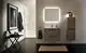 Ideal Standard Badezimmer mit Waschplatz und Schrank, beleuchtetem Spiegel, Handtuchhalter und Dusche. Dunkler Boden und hängendes Handtuch ergänzen das Design.